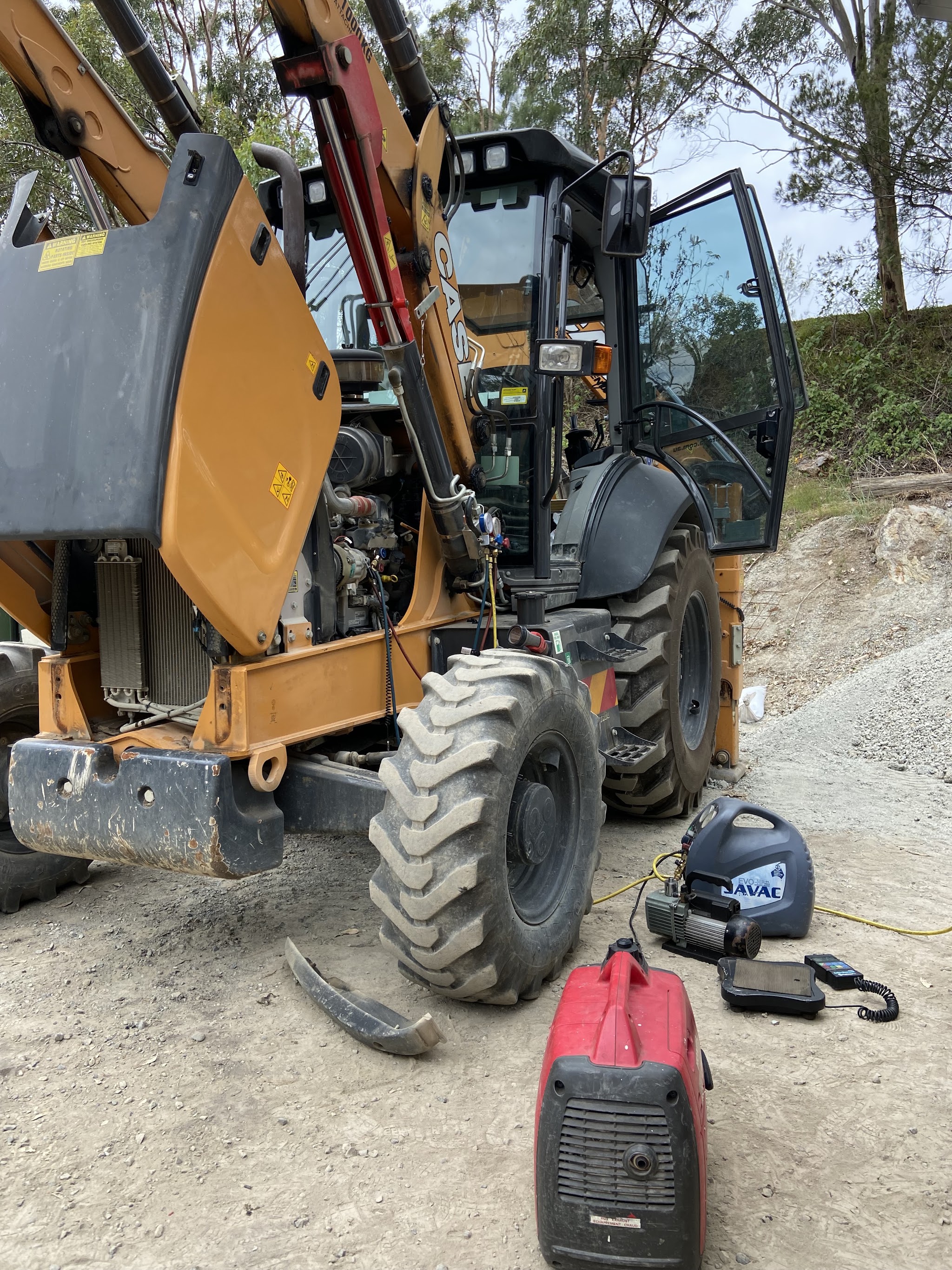 CASE backhoe loader on a dirt site with side panels open, gauges connected and a vacuum pump on the ground